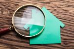 Closeup Of Magnifying Glass And Green Paper House On Wood