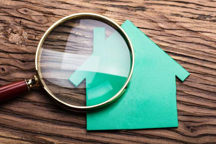 Closeup Of Magnifying Glass And Green Paper House On Wood