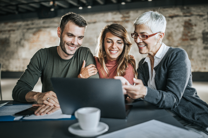 Happy couple and their real estate agent using laptop in the office.