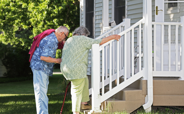 Elderly senior couple arriving home. He is helping her climb slowly up their back porch steps.